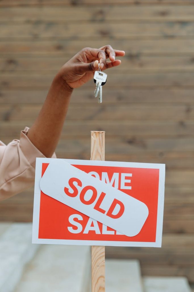 A hand holding keys above a sold sign in a real estate environment, symbolizing a completed property sale.